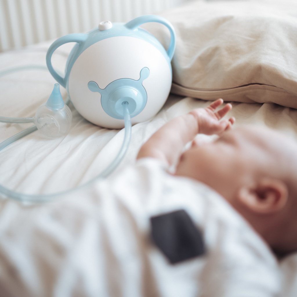 Alvó csecsemő, mellette kék Nosiboo Pro elektromos orrszívó